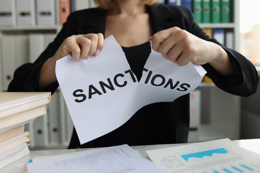 Businesswoman tears up sheet of paper with sanctions inscription
