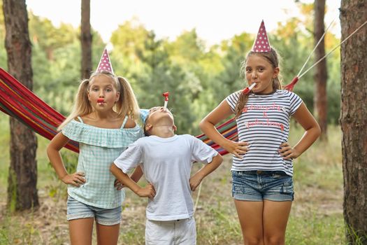 birthday, childhood and celebration concept - happy kids blowing party horns