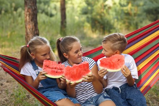 children eat watermelon and joke, in the fresh air, sitting on a hammock