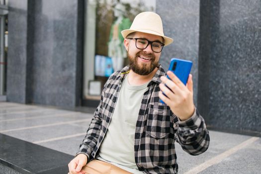 Bearded man doing video call on smartphone outdoor - video connection and technologies concept
