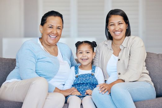 Happy mature grandmother relaxing with her granddaughter and adult daughter at home. Cheerful little hispanic girl sitting on the couch together with her mother and grandmother