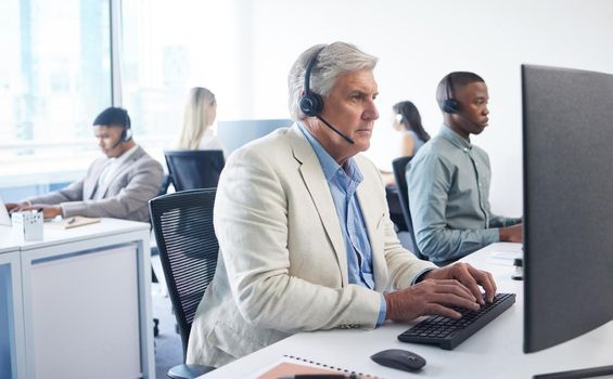 Ive never met a query I cant handle. Portrait of a mature businessman using a headset and computer in a modern office.