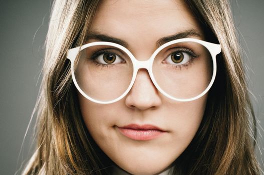 Being a geek aint easy. Shot of a young woman wearing retro glasses against a studio background.