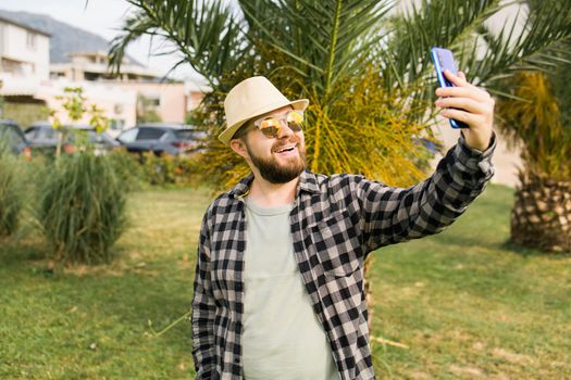 Man taking selfie portrait over palm tree background - Happy millennial guy enjoying summer holidays in city - Youth and technologies