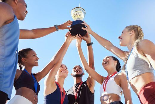 A diverse team of athletes celebrating a victory with a golden trophy and looking excited. A fit and happy team of professional athletes rejoicing after winning an award at an athletic sports event