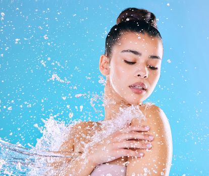 Deadly fresh. Shot of a beautiful young woman being splashed with water against a blue background.