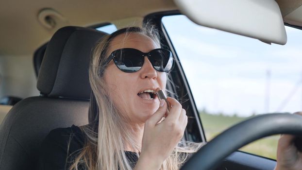 A woman paints her lips while driving.