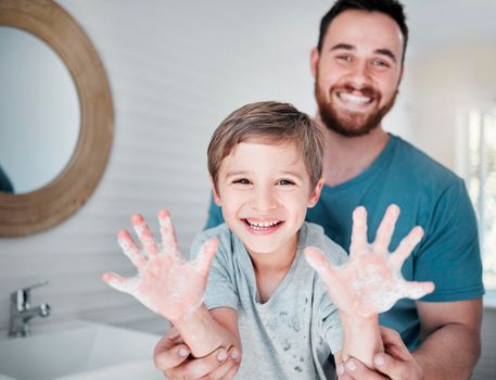 Germ free hands are happy hands. Portrait of a boy holding up his soapy hands while standing in a bathroom with his father at home.