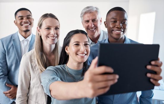 Gather around for a team photo. Shot of a group of businesspeople taking selfies together on a digital tablet in an office.