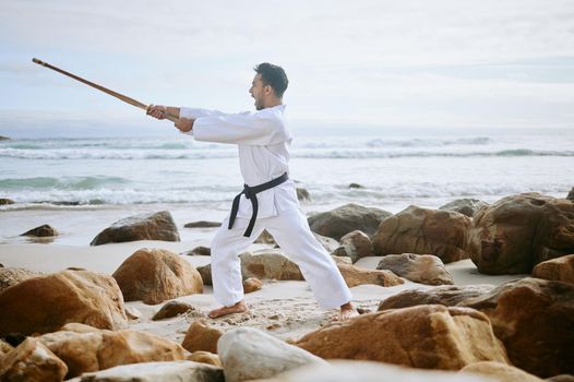 Your spirit is the true shield. Shot of a young martial artist practising karate with a wooden katana on the beach.