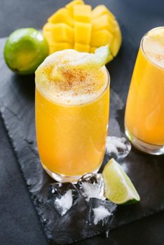 Mango juice on a dark background. Summer drink with ice and slices of mango and lime.