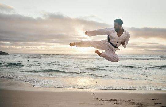 Keep calm and kick on. Shot of a young martial artist practising karate on the beach.