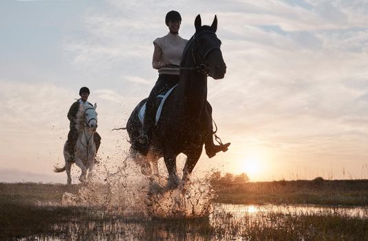 Sunset is our favourite time of the day to ride. Shot of two young women out horseback riding together.