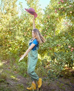Cheerful farmer feeling optimistic and fulfilled for harvest season of fresh organic fruit. One excited energetic happy young woman jumping for joy on sustainable apple orchard farm on sunny day.