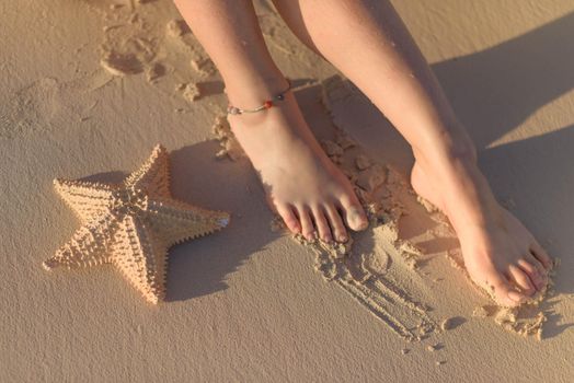 Women's feet and starfish on yellow sand.
