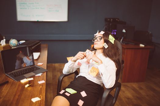 Tired young businesswoman with pasted note-cards. Thoughtful Caucasian lady sitting at armchair in office. Side view. Multitasking concept. Tinted image