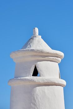 White chimney or bell tower designed on the roof of a house or building against a clear blue sky background with copyspace. Construction of exterior architectural structure at a historical monument