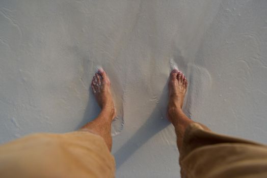 Female legs on a sandy beach with white sand and algae.