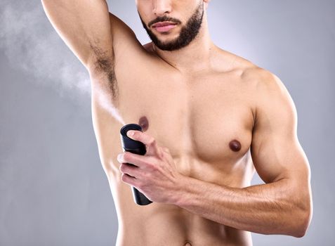 I want to smell good. Studio shot of a young man spraying deodorant on his armpit.