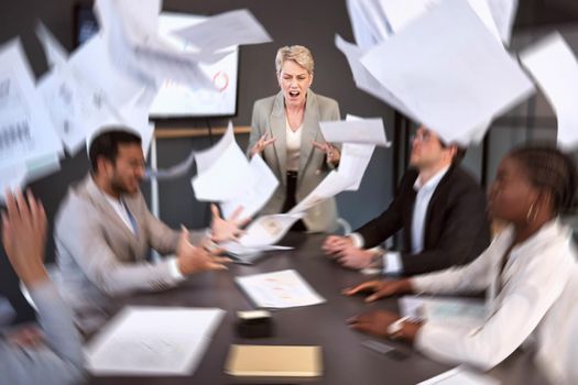 She gets pissed off when things dont go her way. a senior businesswoman screaming in anger during a meeting in an office with paperwork falling around.