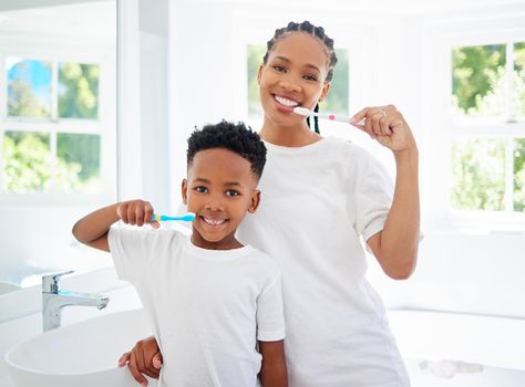 Taking care of teeth and gums is crucial for longterm health. Portrait of little boy and his mother brushing their teeth together in a bathroom at home.