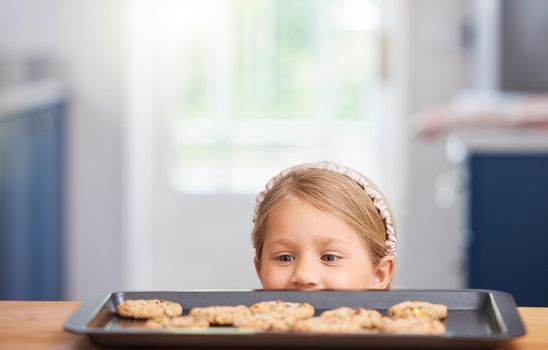 These look delicious. an adorable little girl looking at cookies on a baking tray.