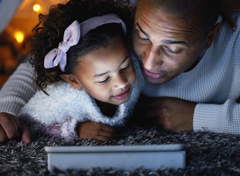Teach them lots, love them always. an adorable little girl using a digital tablet with her father during bedtime at home.