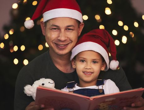 Lets get into the story of Christmas. a young father and daughter reading a book during Christmas time at home.