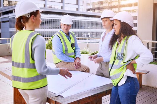 Communication is important in the construction industry. a group of construction workers looking over building plans while standing on site outside.