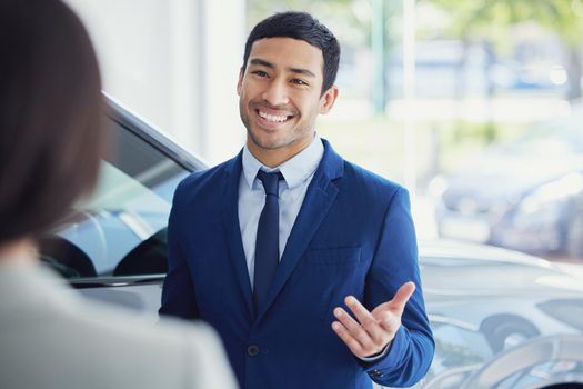 These are your options. a handsome young male car salesman talking to a female customer on the showroom floor.