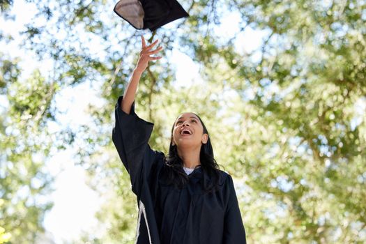 Its that time. an attractive young female graduate throwing her cap into the air outside.