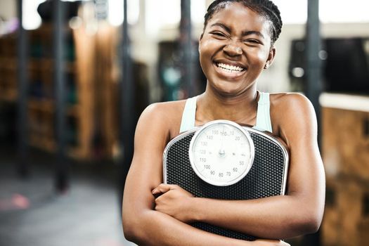 The scale is my best friend during my weight loss journey. an attractive young woman standing alone in the gym and holding a scale after her workout.