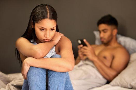 Is it me. a young woman sitting on her bed and feeling upset while her boyfriend uses his cellphone behind her.