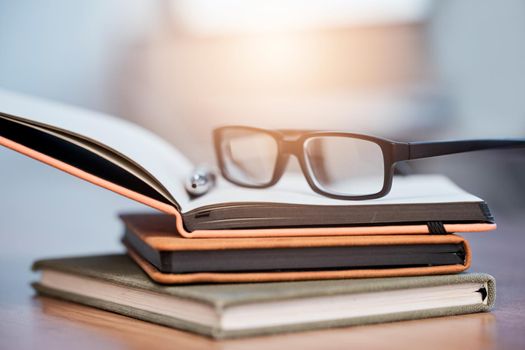 What plans have you made towards your goals. Closeup shot of a pair of spectacles on a pile of notebooks on a table.