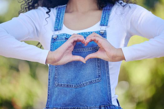 Respond with love. an unrecognizable woman forming a heart shape while standing outdoors.