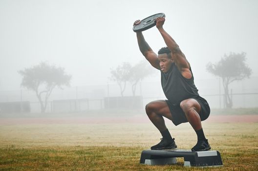 Step up or youll fall behind. a muscular young man exercising on a step with a weight plate outdoors.