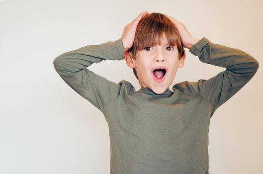 I cant believe this. Studio shot of a cute little boy reacting to something surprising and posing against a wall.