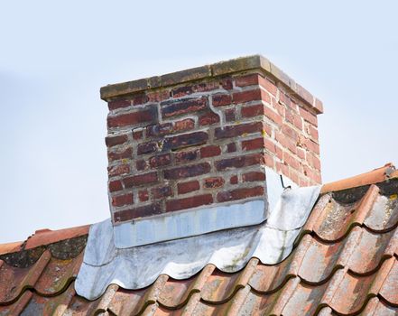 Red brick chimney designed on roof of house or building outside against a sky background. Construction frame of escape chute built on rooftop for smoke and heat ventilation from a fireplace or oven
