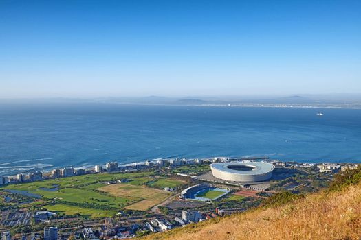 Above panoramic photo of a the central business district of Cape Town, Western Cape, South Africa. A busy peninsula where land meets sea against a cloudscaped blue sky. A beautiful mountainside city