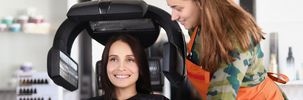 Young lady under hairdressing machine while looking in mirror