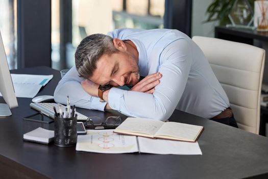 A power nap could be the boost youre looking for. a mature businessman having a nap at while sitting at a desk in a modern office.