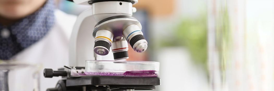 Woman scientist explore purple sample under microscope in laboratory