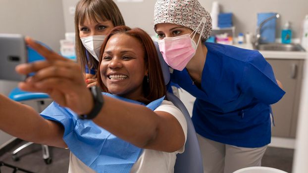 A black woman patient takes a selfie with two dentist woman at the dental clinic