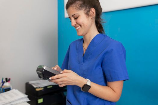 A dental clinic's employee smiles while looking at the dataphone to check if payment, for the services given to a good client has made correctly