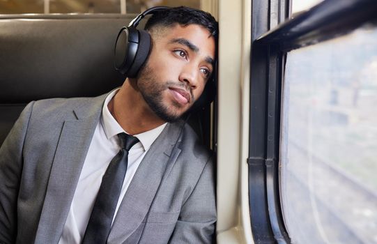 In deep contemplation during his commute. a young businessman wearing headphones while staring out the window on a train during his commute.