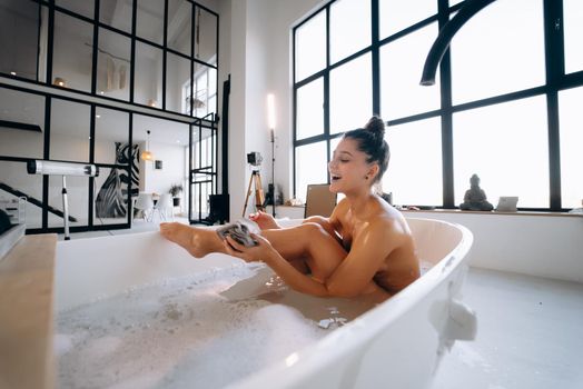 Beautiful woman rubbing her leg with sponge while taking bath