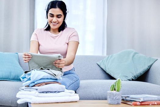 Have fun with your chores. a young woman folding clothes at home.