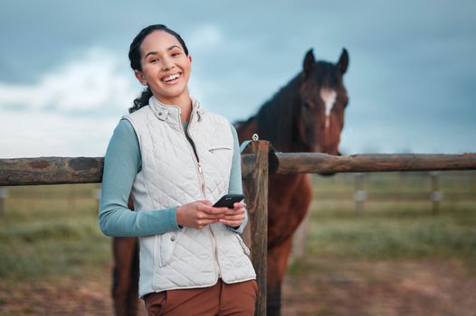 Friends in a field. Portrait of an attractive woman using her cellphone while posing with a horse in an enclosed pasture on a farm.