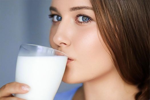 Happy young woman drinking milk or protein cocktail from glass, healthy drink, diet and wellness