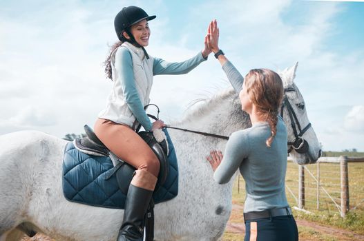 Youre doing so great. an attractive woman and her instructor sharing a high five while out riding in the field.